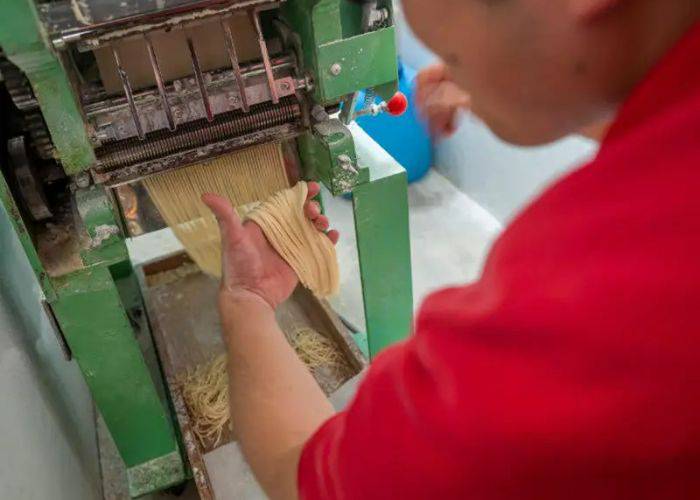 A person gently pulling fresh ramen noodles from a noodle-making machine.